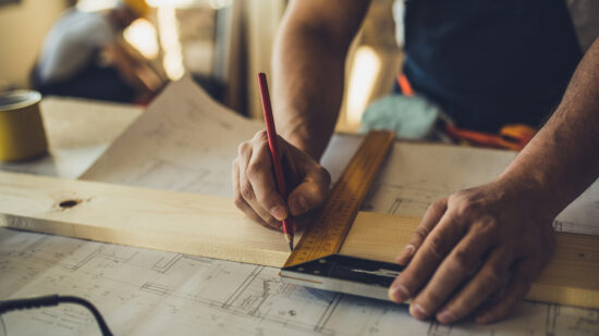 Close up of unrecognizable worker drawing on wood plank.